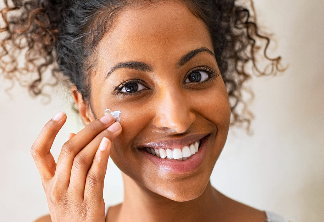 woman smiling while applying skin care product on face