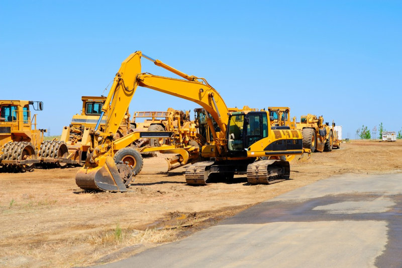 Heavy construction equipment sits idle lined up along a new asphalt road