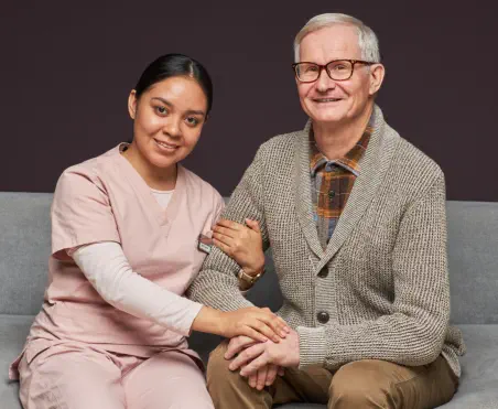 a female caregiver and an elderly man smiling together