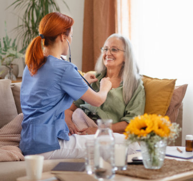 Nurse examining senior patient with stethoscope at her home.