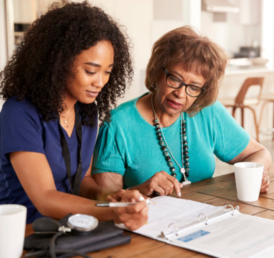 Female healthcare worker filling in a form with a senior woman during a home health visit